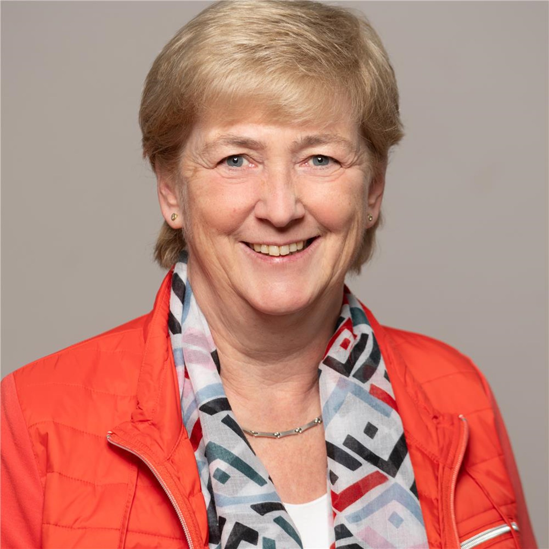 Portraitaufnahme von einer lächelnden Frau mittleren Alters in rot-oranger Jacke mit Halstuch